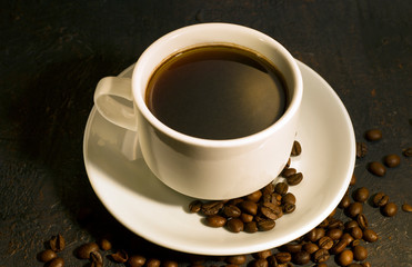 Cup of coffee on a black background with scattered coffee beans.