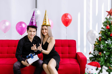 Attractive young couple celebrate Christmas and New Year together. Man giving present gift box to woman, looking at camera