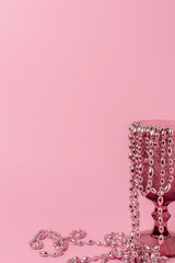 glass with a pattern on a pastel pink background. Beads hang from the edge of the cup and partially lie on the table. All objects and background are pink. Minimalism. Copy space. vertical photo.