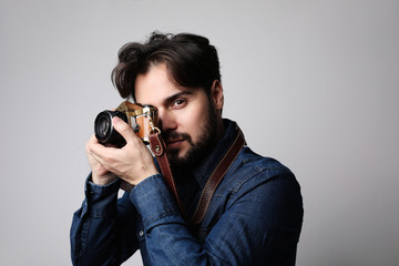 Young bearded hipster posing in the studio and holding his vintage camera.