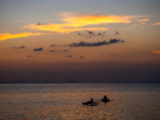 Silhouettes of people on sup boards in the rays of the setting sun against a background of clouds. Koh Phangan. Thailand.