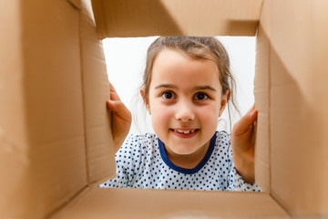 kid girl age 7 year unpacking and opening carton box, and looking inside with surprise
