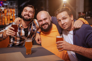Group of happy male friends smiling to the camera while drinking beer together at the pub