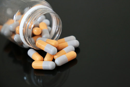 Pills in a bottle, medication in capsules on a dark glass table. Concept of pharmacy, antibiotics, vitamins