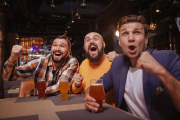 Group of friends scraming, watching football game at beer pub. Male soccer fans looking excited, celebrating victory of their favorite team