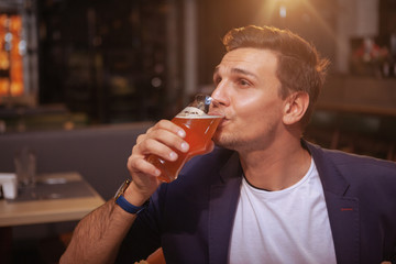 Handsome businessman relaxing at beer pub after working day. Attractive elegant man sipping beer at the bar