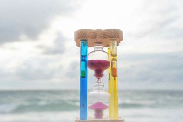 The hourglass passing time on the beach The hourglass in front of the bright blue sky with white...