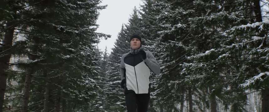 Caucasian athlete or sportsman runs fast along through winter forest in cold weather. Endurance exercise cardio training, outdoor workout. Anamorphic shot