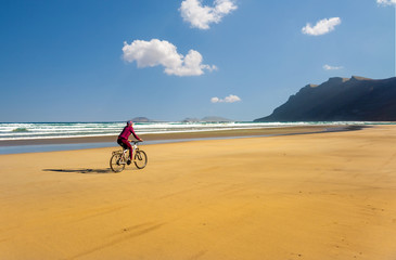 Sporty young woman ride bicycle on sand Famara beach. Lanzarote Canary Island