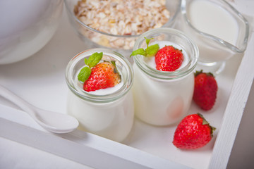 Two portions natural homemade yogurt in a glass jar with fresh strawberry and muesli nearby