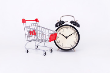 Shopping cart and classic alarm clock on white background. Sale time buy mall market shop consumer concept. Selective focus.