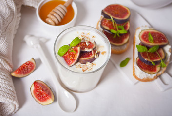 Yogurt with muesli and fig fruit in a glass, sandwich with cream cheese, figs and honey on the white treay. Healthy food concept.
