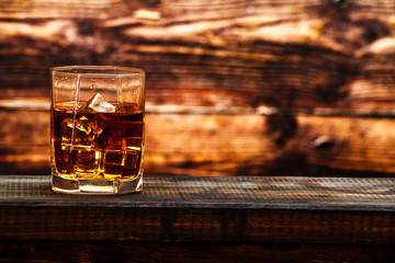 Whiskey with ice or brandy in a glass and a square carafe on an old wooden background. Whiskey with...