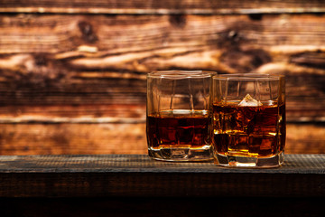 Whiskey with ice or brandy in a glass and a square carafe on an old wooden background. Whiskey with ice in a glass. Whiskey or cognac. Selective focus.
