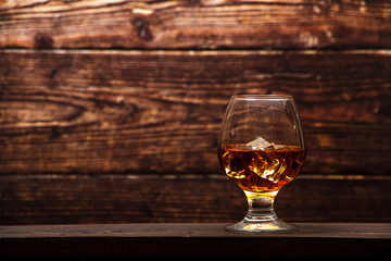 Whiskey with ice or brandy in a glass and a square carafe on an old wooden background. Whiskey with ice in a glass. Whiskey or cognac. Selective focus.