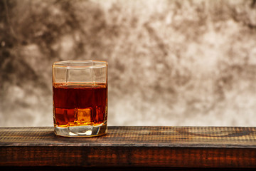 Whiskey with ice or brandy in a glass on a background of gray concrete on an old wooden table. Whiskey with ice in a glass. Whiskey or brandy. Selective focus.