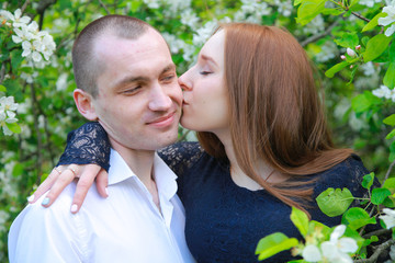 Young couple in fruit orchard apple garden with blossom branches walking together and have a date