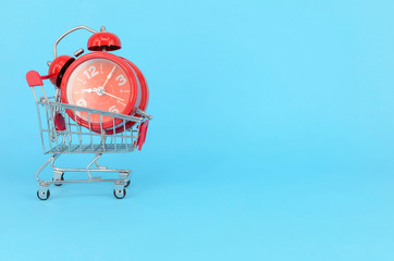 Shopping cart and classic alarm clock on blue background. Sale time buy mall market shop consumer...