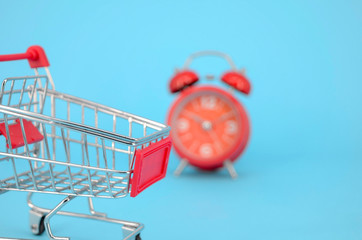 Shopping cart and classic alarm clock on blue background. Sale time buy mall market shop consumer...