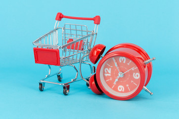 Shopping cart and classic alarm clock on blue background. Sale time buy mall market shop consumer...