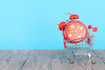 Shopping cart and classic alarm clock on blue background. Sale time buy mall market shop consumer...