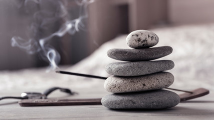 Concept of relax or meditation. Pyramid of zen stones, burning incense stick, bedroom interior.