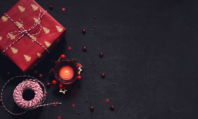 Black festive background with red decoration, candle and gift, Chrtistmas and new year greeting card with place for text