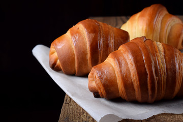 Golden croissants of yeast dough on the edge of the wooden table against black background
