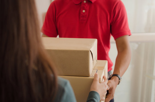 Young Asian Woman Customer Receive Parcel Post Box From Home Delivery Service Man In Red Uniform At Home, Express Home Delivery Service, Cargo Shipping, Transport Logistics And Online Shopping Concept