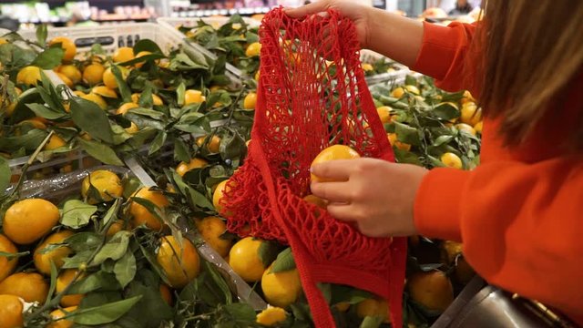 Young woman picking veggies and fruits in supernarket in mesh organic shopping bag, zero waste