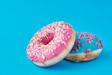 Two donats decorated sprinkles and icing on a blue background