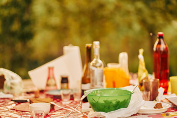 outdoor dining table in a outdoor summer house laden with dishes, bottles and leftover food. dinner in the garden in nature.