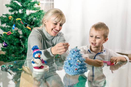 grandmother teaches a little boy to make decorations for Christmas (New Year) fir tree with his own hands