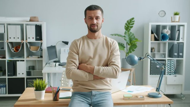 Portrait of successful young businessman smiling looking at camera in office standing with arms crossed happy. People, business and workplace concept.