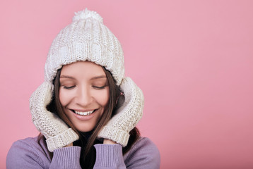 Smiling beauty girl with closed eyes in a winter white knitted hat and white mittens