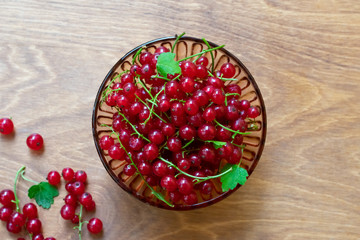 Transparent bowl full of juicy red current berries on wooden table. Freshly picked ripe red currants in plate on dark rustic wooden table.