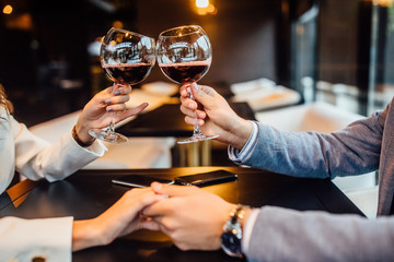 Cropped image, romantic couple holding glass of red wine and enjoying in conversation.