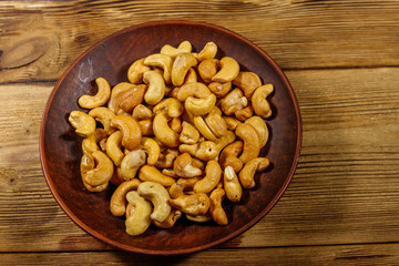 Ceramic plate with roasted cashew nuts on a wooden table. Top view