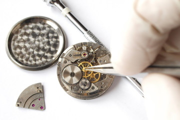 watchmaker working on vintage watch mechanism taking small gear with tweezers