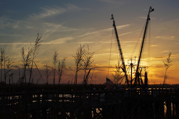 A docked shrimp boat with see oats in foreground and sunset in background.  On the river in Darien, GA.