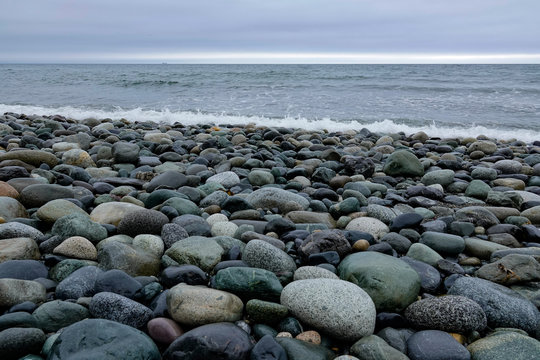 This rocky beach on Puget Sound is very difficult to walk on. The tide is out revealing the smooth and beautifully colored stones. Low angle with level horizon at top third. It is a cloudy day. - Powered by Adobe