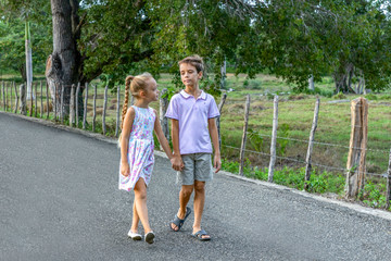 A little girl and a boy walking in the street, holding hands smiling and looking each other, friendship and first love concept 