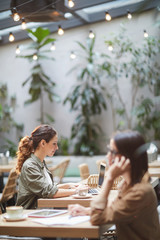 Side view portrait of elegant businesswoman using laptop while sitting at table in outdoor cafe, copy space