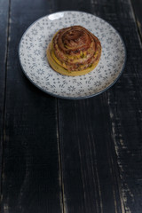 Vertical shot of cheese and dill bread bun on plate standing on black wooden background. Tasty unhealthy food. Diet, nutrition, eating habits concept. Place for text. 