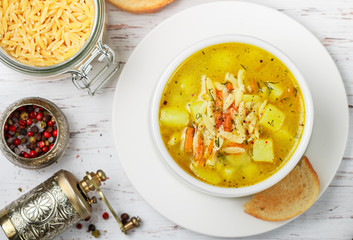Minestrone. Chicken soup with potatoes, carrots and pasta Orzo in a white plate on a wooden table. Minestrone.  Mediterranean (Italian) cuisine. Selective focus