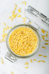 Orzo, a form of pasta shaped like rice in a glass jar on a marble surface. Selective focus