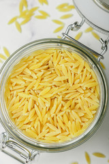 Orzo, a form of pasta shaped like rice in a glass jar on a marble surface. Selective focus