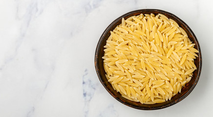 Orzo, a form of pasta shaped like rice in a ceramic bowl on a marble surface. Selective focus, copy space and top view