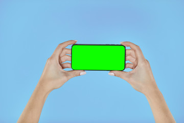 Woman hands holding smartphone with green screen on a blue background. Mock up mobile