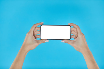 Woman hands holding smartphone on a blue background. Smartphone mockup with white screen